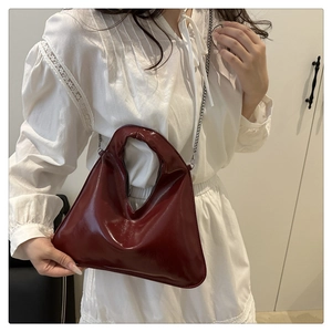 Detail of burgundy bucket bag with round cutout handle and silver chain strap
