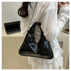 Close-up of black glossy patent leather handbag with delicate metal chain strap details