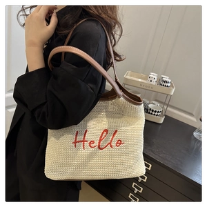 Detail of woven straw tote bag with red Hello embroidery and brown leather shoulder strap