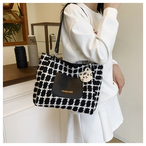 Detail of tweed checkered tote bag with leather pocket and white cat plush charm accessory