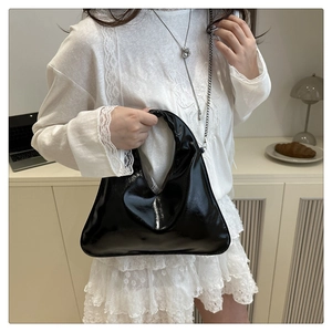 Detail of a chic black glossy triangle bag with elegant metal chain strap on a model