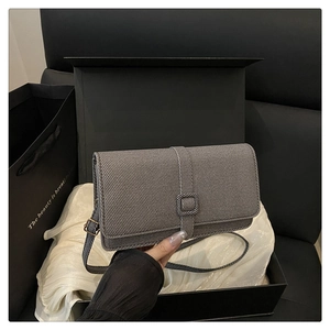 Detailed view of gray crossbody bag with textured fabric and flap on white silk in a gift box
