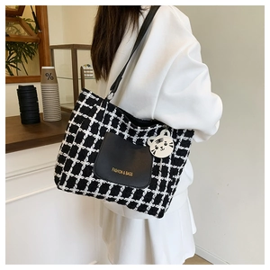 Detail of checkered tweed tote bag featuring a black leather pocket and tiger charm