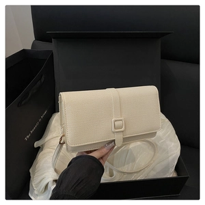 Detail view of a beige textured crossbody bag with square buckle and adjustable strap
