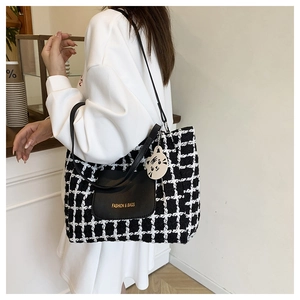 Detail of checkered tweed tote bag featuring black leather pocket and cute cat charm
