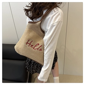 Detail of woven straw tote bag with red Hello embroidery and brown leather straps