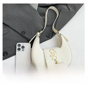 Detalle del bolso de media luna blanco con hebilla dorada y borla junto a un móvil