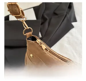 Detail of khaki suede saddle bag with gold metal hardware, rivets, and long side tassels