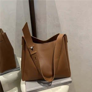 Brown leather tote bag with adjustable strap shown on a white pedestal in a minimal room