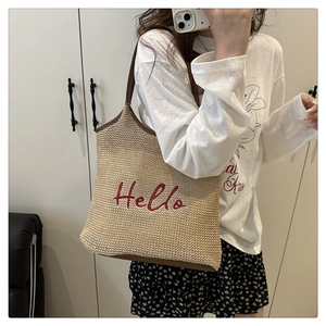 Detail of straw woven tote bag featuring red Hello embroidery and brown leather trim