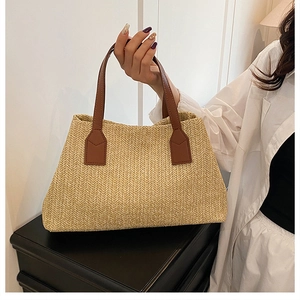 Close-up detail of a handmade straw woven tote bag featuring brown faux leather handles.