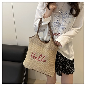 Detail of woven straw tote bag featuring red Hello embroidery and brown leather handles