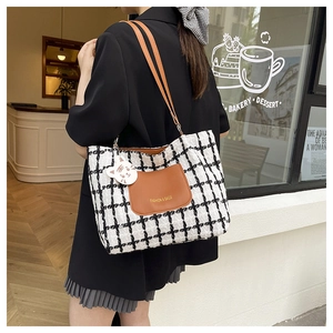 Close-up of black and white plaid tote bag with brown leather strap and cat charm detail