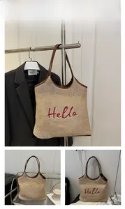 Close-up of woven straw tote bag with red Hello embroidery and brown leather handles