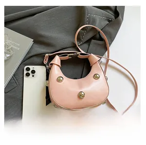 Rosa Halbmond-Handtasche mit Nieten neben einem Smartphone zum Größenvergleich