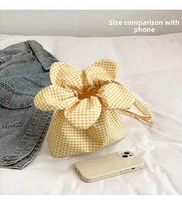 Detail of yellow checkered drawstring bag with flower top showing compact size next to a phone