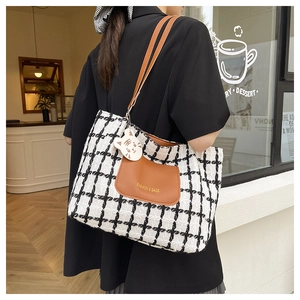 Detail of checkered tote bag with brown leather pocket and cute cat keychain charm