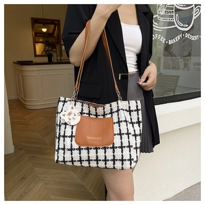Detail of plaid tote bag featuring a brown leather pocket and a cute cat charm accessory