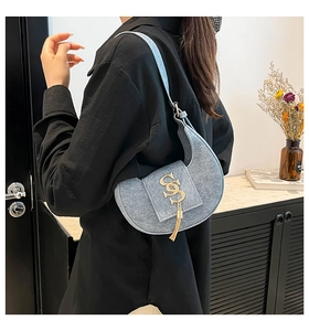 Detalle del bolso de media luna azul claro con hebilla dorada en S y borla en hombro