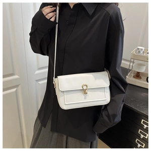 Close-up of ivory leather shoulder bag featuring a gold horseshoe clasp and pebbled texture