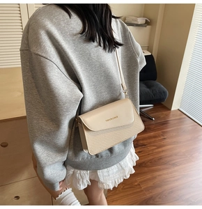 Detail of cream white crossbody bag with woven texture and leather flap on model