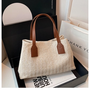 Detailed view of a stylish woven straw handbag featuring brown leather handles in a gift box