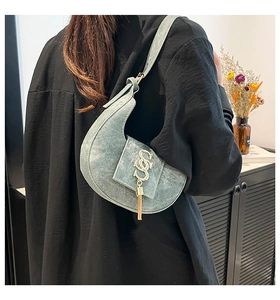 Detalle de bolso medialuna azul con colgante de flecos dorados y logo metálico curvado