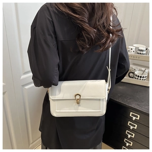 Detail of white leather crossbody bag featuring a unique gold U-shaped hardware clasp