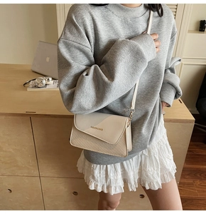Detail of minimalist cream crossbody bag with woven texture and subtle fashion logo