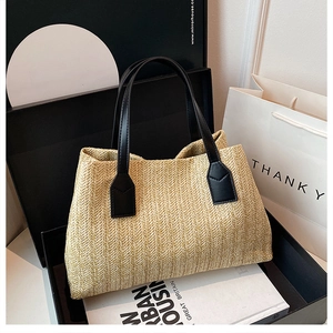 Close-up view of a chic woven straw handbag with black handles displayed in gift packaging