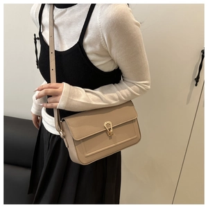 Detail of minimalist beige flap bag featuring a golden teardrop lock and pebbled texture