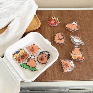 Variety of cute acrylic Capybara phone socket grips on a rustic wooden tabletop