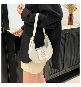 Detalle de bolso medialuna blanco con logo SS dorado y borla llevado por una modelo