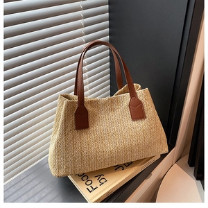 Detailed view of woven straw tote bag with brown handles on minimalist book prop