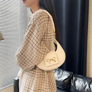 Dettaglio borsa a mezzaluna beige con chiusura a fiocco dorata portata a spalla