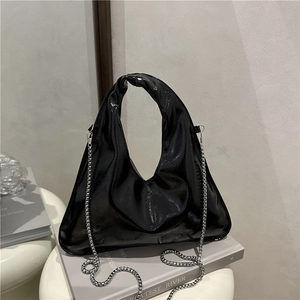 Glossy black triangular tote bag with top handle and silver chain strap on books