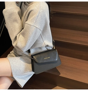 Detail of black crossbody bag with gold text on a stylish leather flap and striped texture