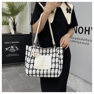 Detail of checkered tote bag featuring white leather pocket and cute cat charm decoration