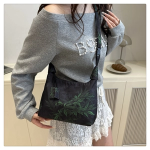 Detail of a Chinese style black bucket bag with green leaf embroidery and crossbody strap