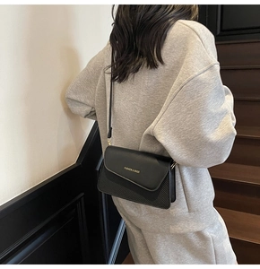 Detail of minimalist black crossbody bag with gold lettering shown on model in street scene