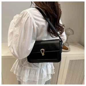Black grain leather shoulder bag with gold horseshoe buckle shown on model in home setting