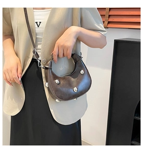 Detail der dunkelbraunen Halbmondtasche mit silbernen Nieten getragen zu einem beigen Blazer