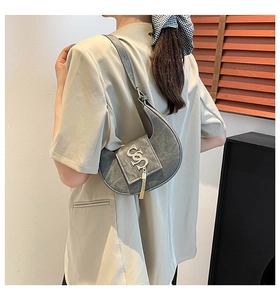 Vista detallada del bolso de media luna gris con logo metálico y elegante borla decorativa