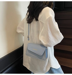 Close-up of a light blue crossbody bag with woven texture and gold adjustment buckle