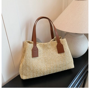 Detailed view of a woven straw tote bag with brown faux leather handles on a table
