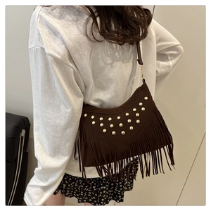 Close-up of bohemian dark brown fringe bag with gold rivets and suede texture