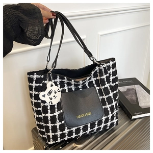 Detail of checkered tote bag with leather pocket and tiger charm on a metal suitcase