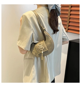 Detalle de bolso medialuna de cuero gris mate con logo metálico dorado y flecos