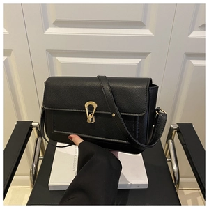 Close-up of black textured leather handbag with elegant gold horseshoe buckle detail