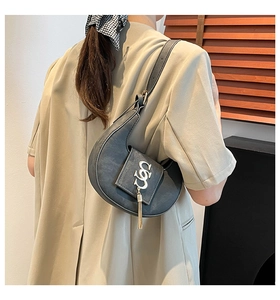 Detalle de bolso medialuna gris oscuro con logo de anillo dorado y flecos metálicos